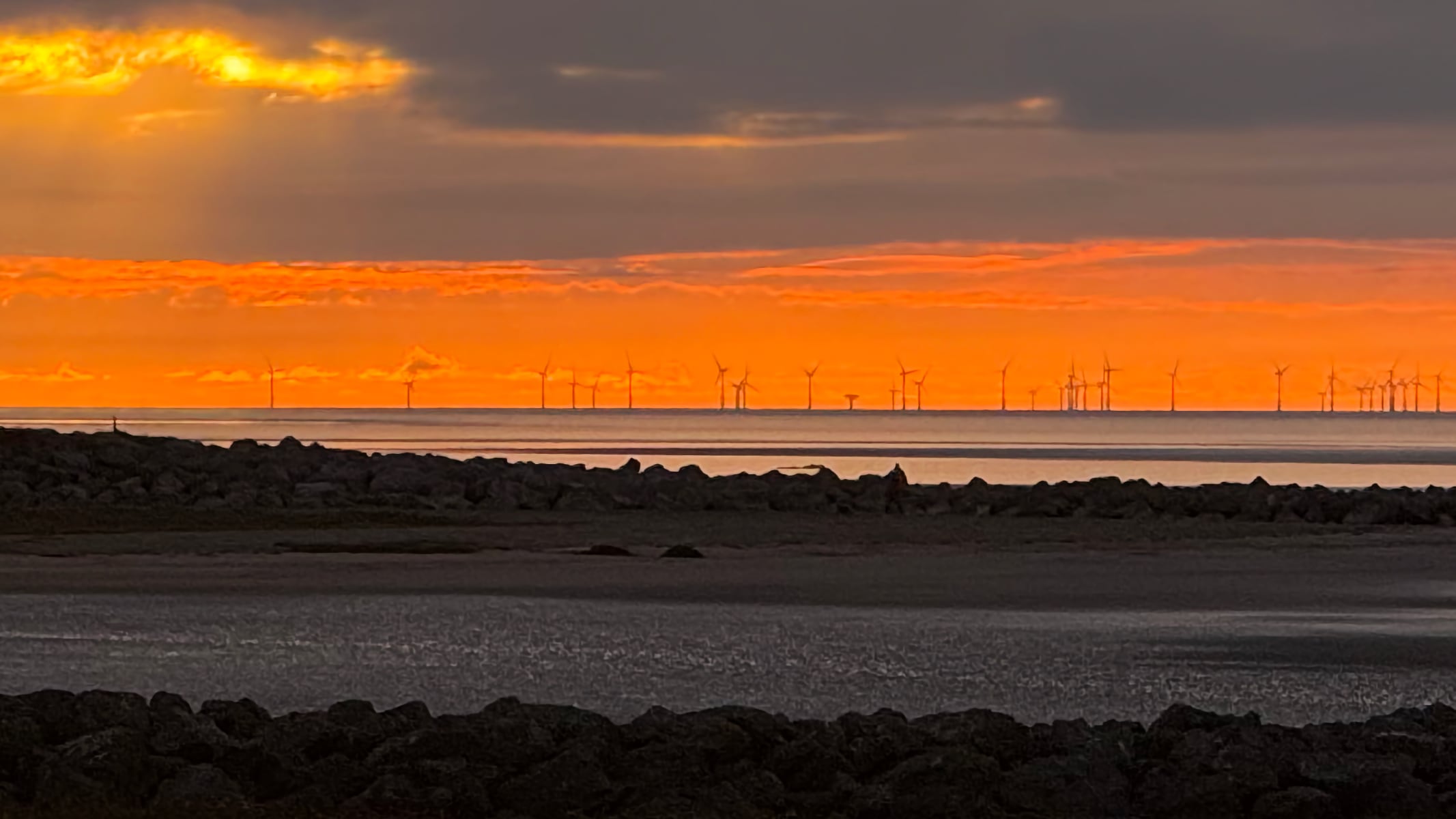 Zoom of wind farm windmills on Morecambe Bay at sunset