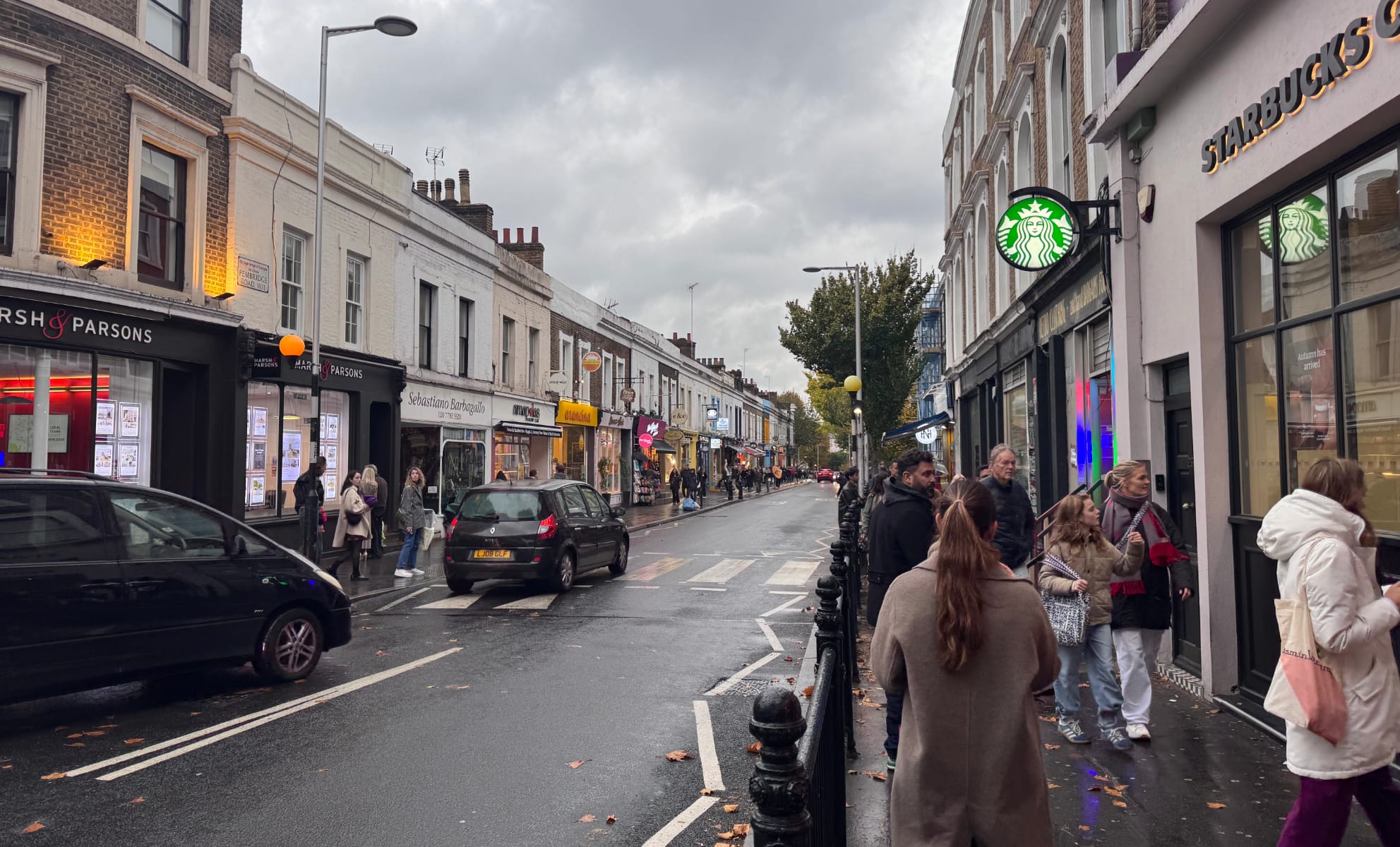 A shopping street in Notting Hill near a Starbucks, with packed sidewalks but mostly empty streets