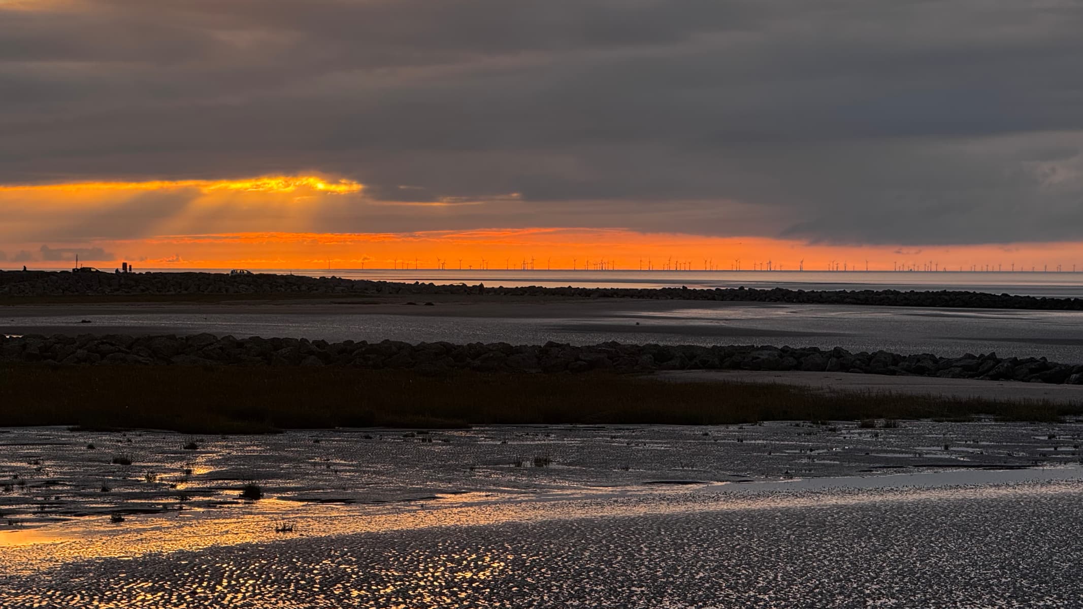 Many wind farm windmills on the horizon of Morecambe Bay at sunset