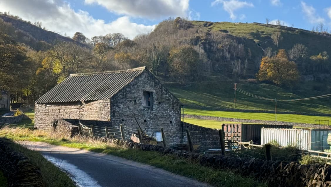 A scenic view of an old stone bard with sunny hillsides behind