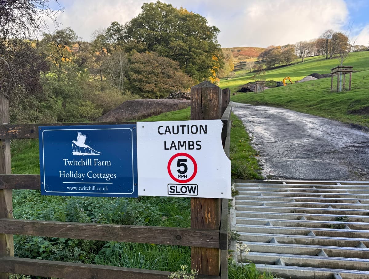 A metal sheep barrier on a road leading into the hills with a sign saying 'Caution Lambs 5mph SLOW'