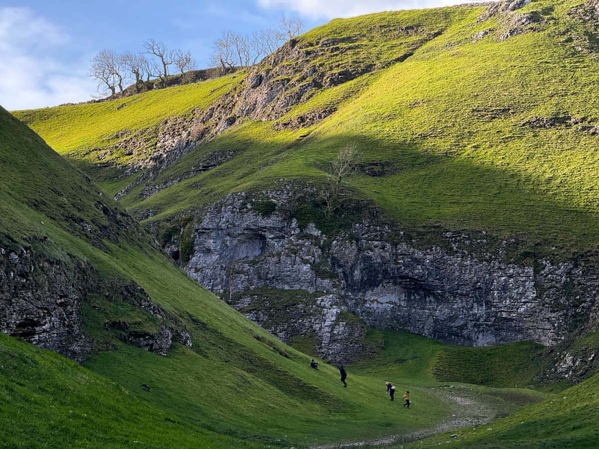 A scenic view of Cave Vale with cliffs below and trees above and bright sunlight on the upper slopes