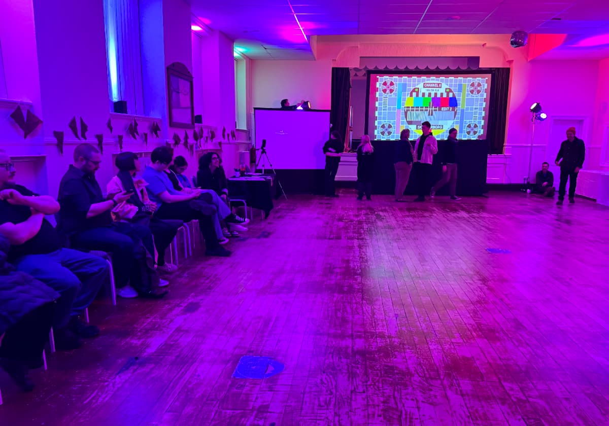 A colourfully lit community hall with some people sitting in chairs by the walls