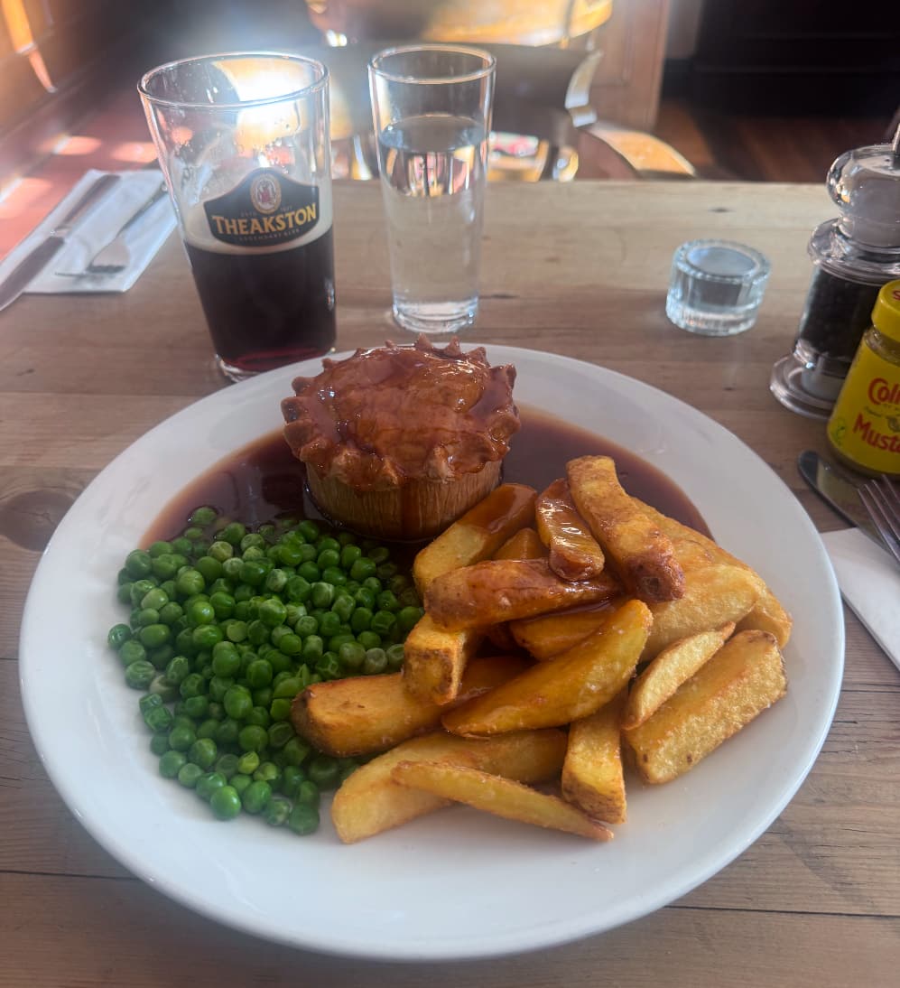 A meat pie with beef dripping chips and peas and gravy, accompanied with a beer