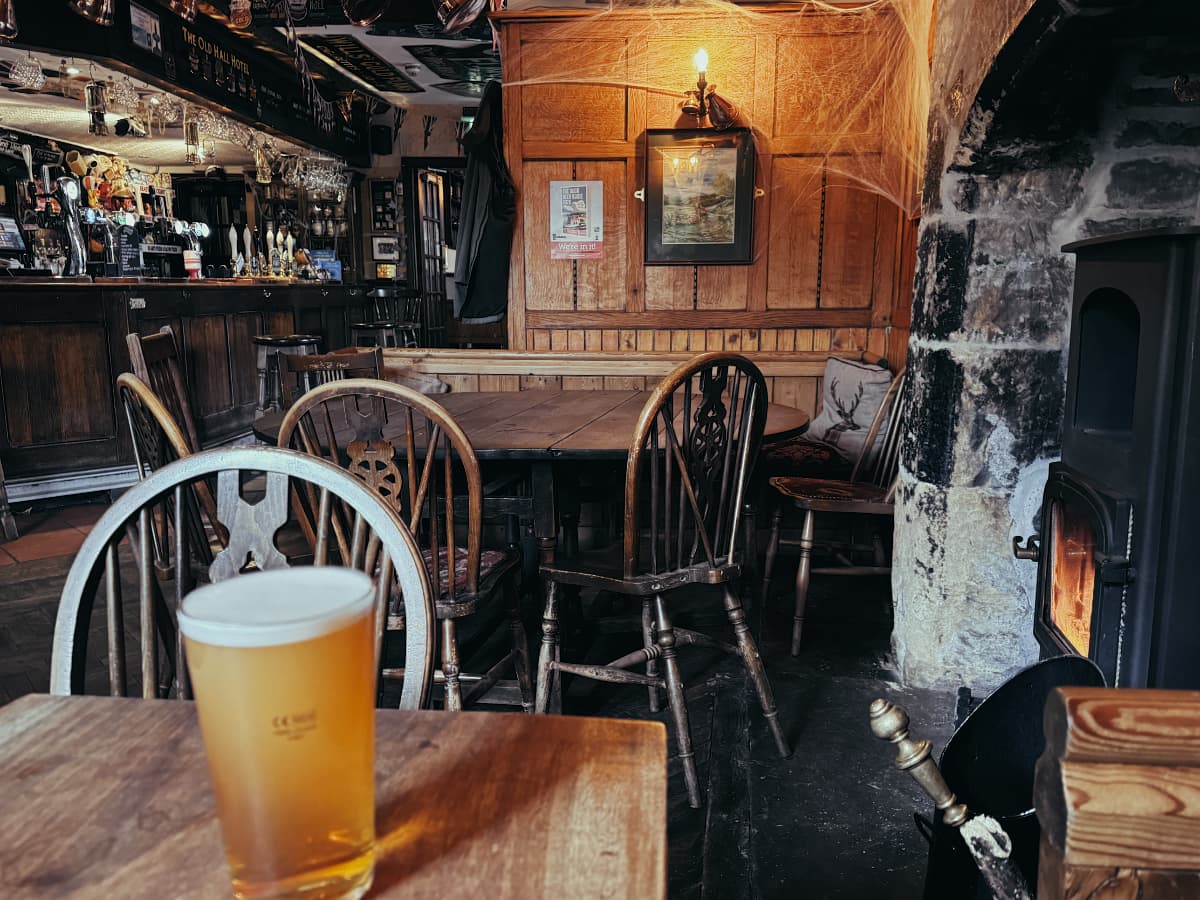 A pint of beer in a rustic looking pub by a wood stove.
