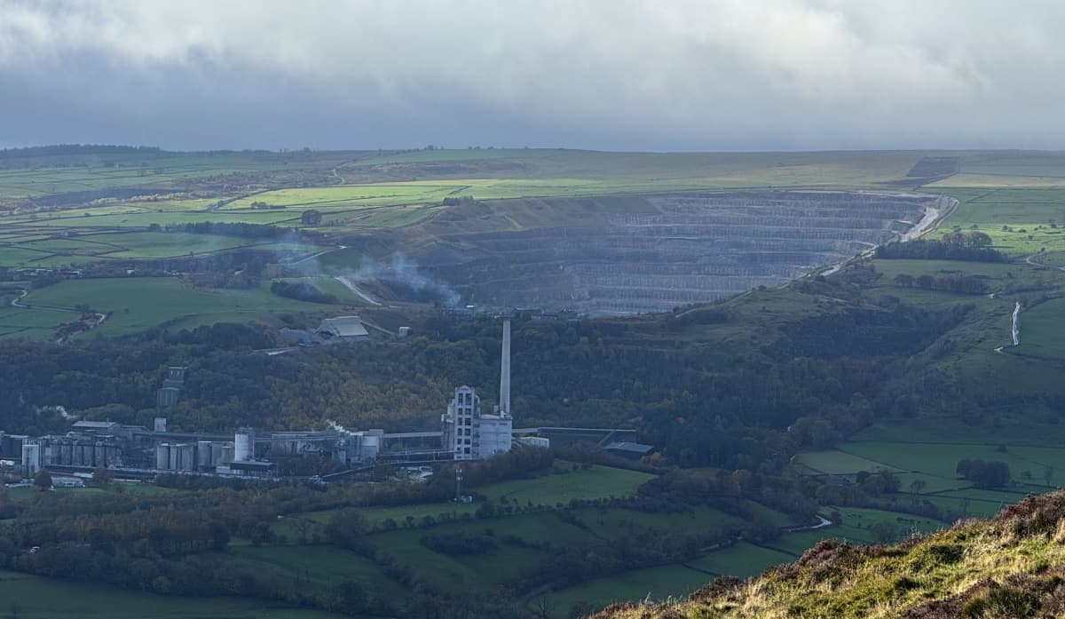 A scenic Peak District hillside with a large open pit cement mine in the middle of it