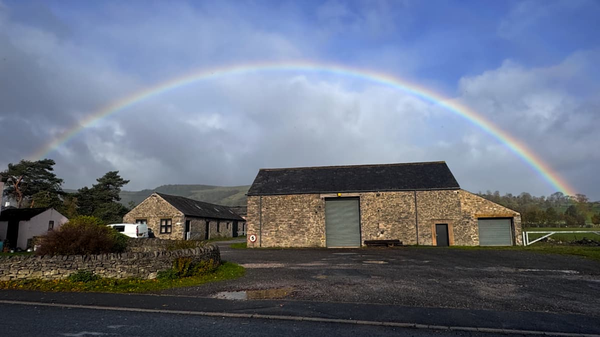 A rainbow over a stone barn/garage by the side of the road