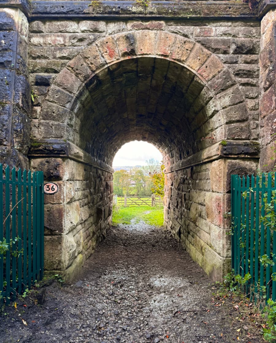 An arched stone tunnel under a railroad track in the Peak District, green hillsides visible on the other side.