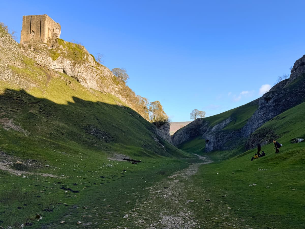 Grassy rocky Cave Vale in shadow with a castle in sunlight above